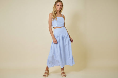 Woman wearing a light blue striped crop top and skirt set on a beige background